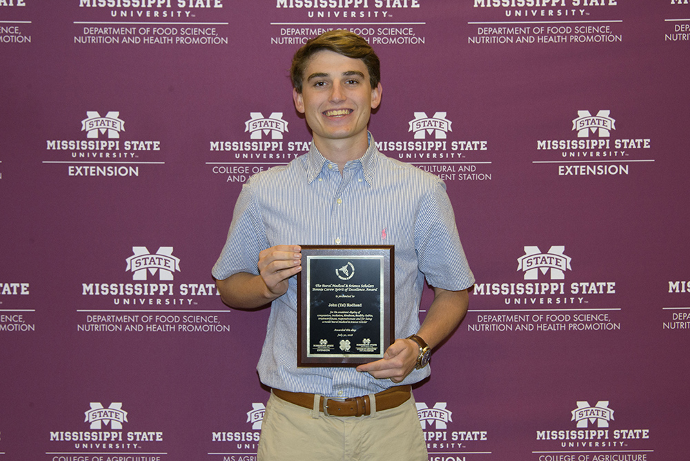 young caucasian male holds award plaque in front of backdrop with various logos
